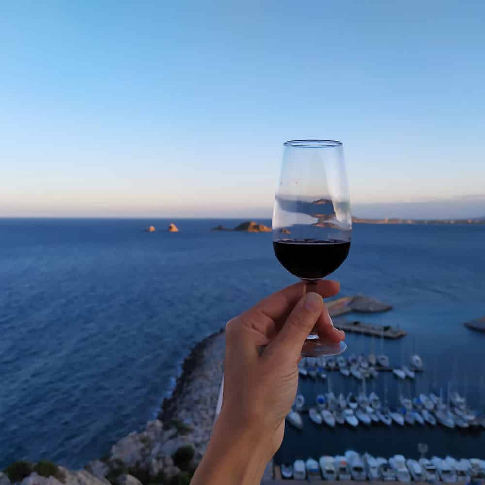 mano de una chica sujetando un vaso de vino italiano en una playa de la isla italiana Cerdeña